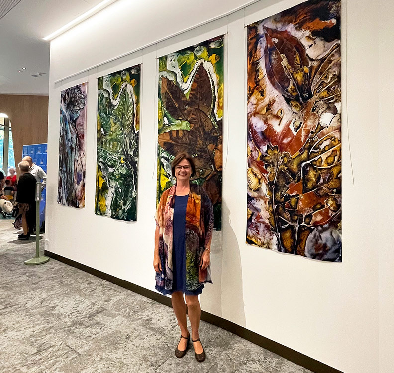 A woman standing in front of 4 large vertical  botanical artworks on fabric 