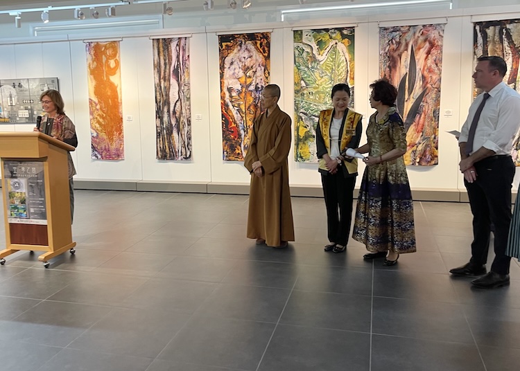 Five people in front of a wall with large vertical art hangings, a woman on the left speaking at the lectern 